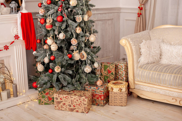 Decorated Christmas tree with gifts. Christmas tree decorated with toys, balls and lights glowing garlands. Cozy xmas interior room with sofa and Christmas tree. Scandinavian style living room - Photo, Image