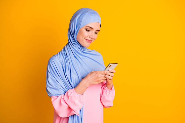 Profile side portrait of pretty focused cheery muslimah wearing hijab dress using gadget comment smm post isolated on bright yellow color background - Φωτογραφία, εικόνα