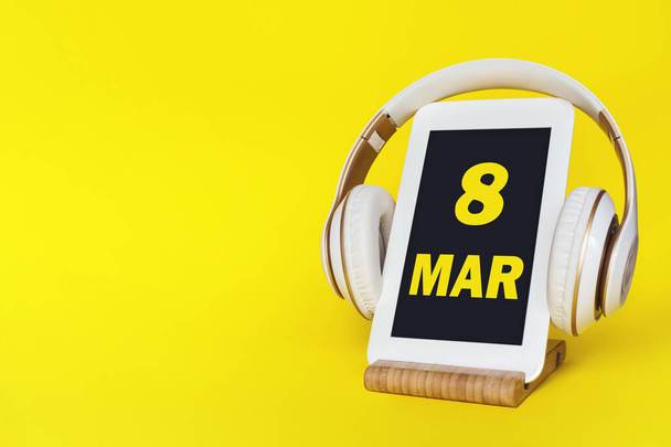 3月8日。月の8日、カレンダーの日付。黄色の背景にスタイリッシュなヘッドフォンとモダンなタブレット。テキスト用のスペース。概念教育技術ライフスタイル。春の月、その年のコンセプトの日 - 写真・画像