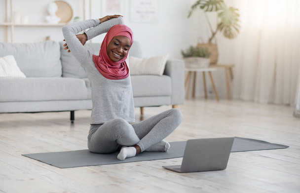Zdrowy styl życia. czarny muzułmanin kobieta robi fitness gimnastyka z laptop w domu - Zdjęcie, obraz