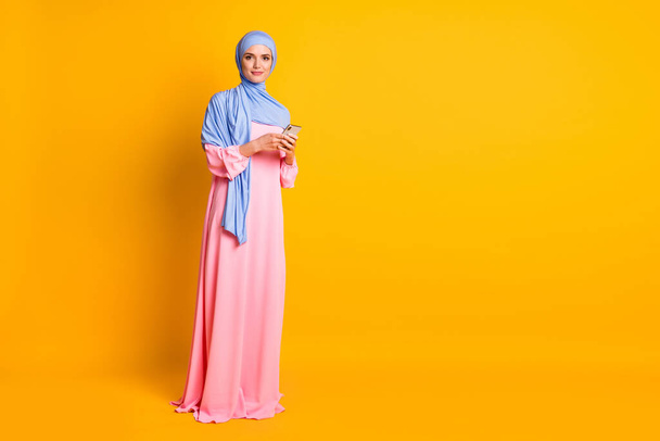 Full length body size view of nice pretty elegant muslimah wearing hijab dress using device blog isolated on bright yellow color background - Fotó, kép