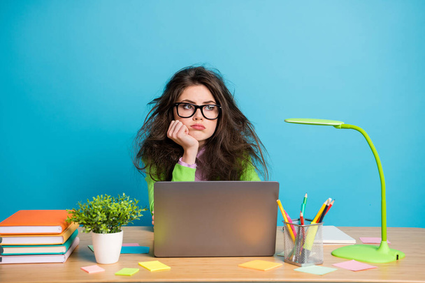 Portrait of bored high school girl sit desk look copyspace wear green shirt isolated over blue color background - Foto, immagini