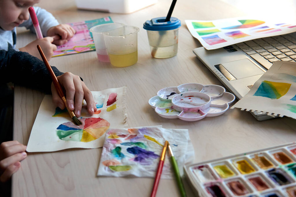 Children painting pictures with watercolor paints during art lesson. Pupils are concentrating on drawing with brush. Watercolor color wheel and palette. Color theory beginner hobby lessons - Fotoğraf, Görsel