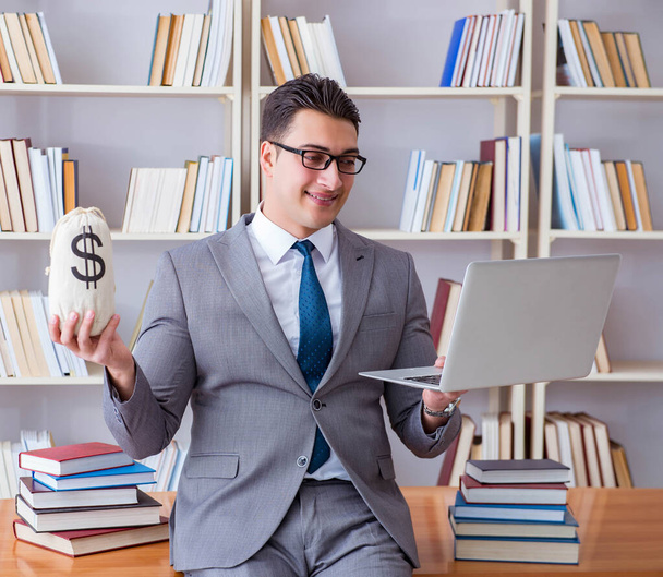 Бизнесмен в библиотеке с мешком денег и ноутбуком - Фото, изображение