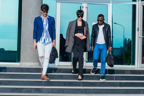 Jeunes gens multiethniques modernes en tenue formelle discutant affaires tout en marchant à l'extérieur de l'immeuble de bureaux - Photo, image