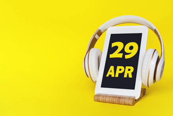 April 29th. Day2 9 of month, Calendar date. Stylish headphones and modern tablet on yellow background. Space for text. Concept education, technology, lifestyle. Spring month, day of the year concept - 写真・画像