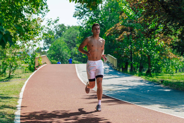 Silný atraktivní muž pobíhající venku bez trička v parku - Fotografie, Obrázek