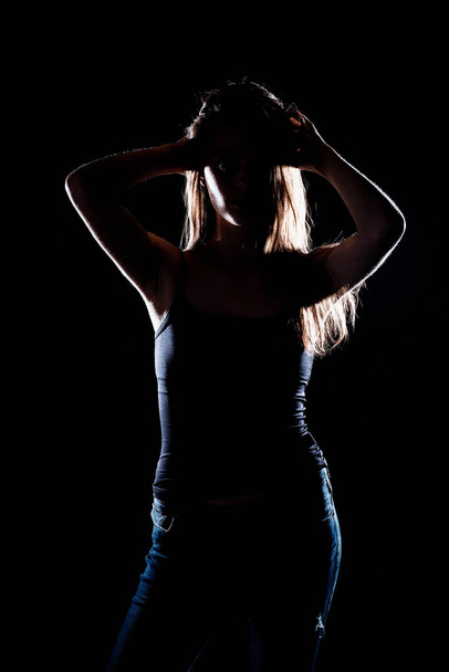 Portret van een vrouwelijk model poserend in trendy denim jeans tegen zwarte achtergrond - Foto, afbeelding