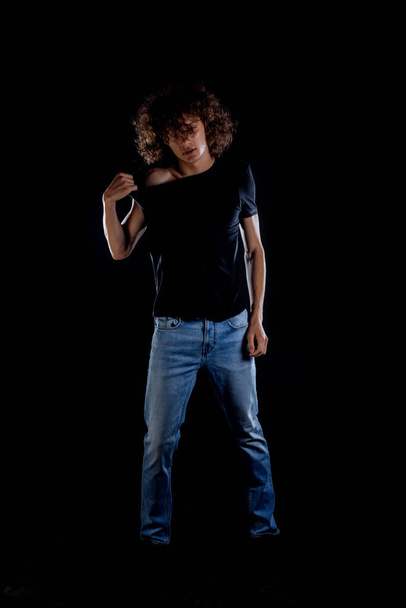 Przystojny młody chłopiec w hipsterskich dżinsach pozując na ciemnym tle - Zdjęcie, obraz