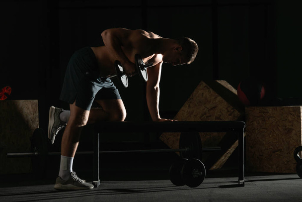 Kafkasyalı atletik bir adam, halterli trisepsi sağ koluyla yatay bir bankta kullanıyor.. - Fotoğraf, Görsel