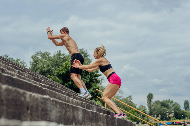 Untere Ansicht von jungen männlichen und weiblichen Athleten, die auf der Außentreppe nach oben springen - Foto, Bild