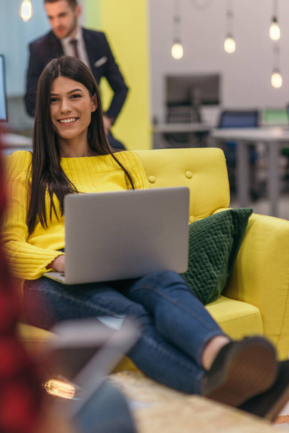 Красива бізнес-леді (працівник) сидить на жовтому дивані, працюючи на ноутбуці в стартап-компанії
. - Фото, зображення