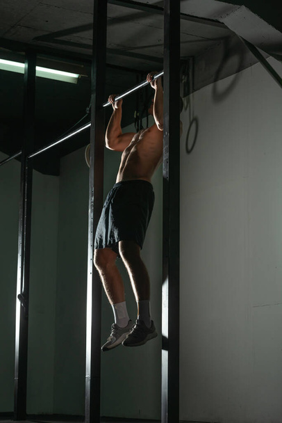 Όμορφος bodybuilder κάνει pull-ups σε οριζόντια γραμμή σε ένα εσωτερικό σύγχρονο γυμναστήριο. - Φωτογραφία, εικόνα