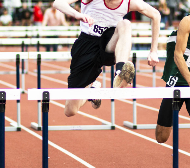 A high school track and field runner is racing in the hurdles during an indoor competition.  - Photo, Image