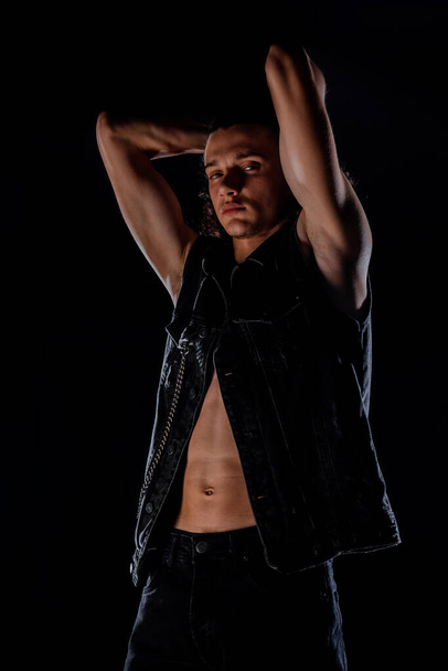 Attractive young stylish man posing in black vest and black denim pants - 写真・画像