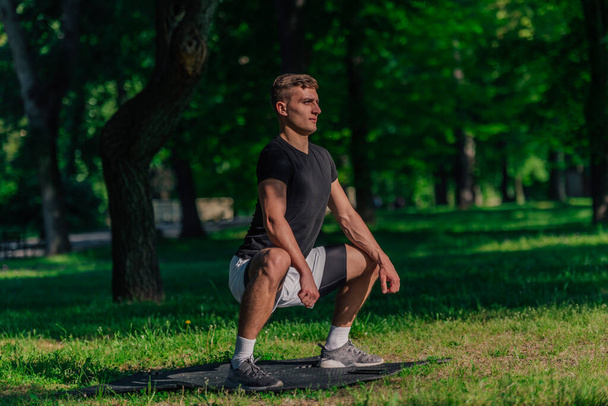 Zdrowy młody człowiek robi na świeżym powietrzu ćwiczenia rozciągające rozgrzewkę na macie fitness - Zdjęcie, obraz