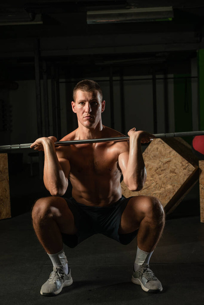 Κοντινό bodybuilder κάνει barbel overshoulder press σε ένα γυμναστήριο, ενώ κάμψη των μυών πορτρέτο του. - Φωτογραφία, εικόνα