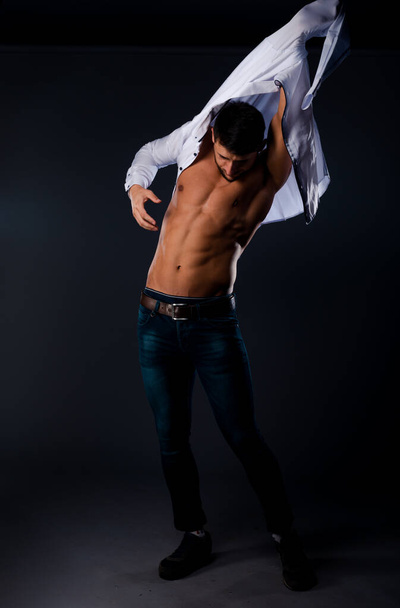 Портрет молодого привлекательного мужчины, одетого в белую рубашку, изолированный на темной стене - Фото, изображение