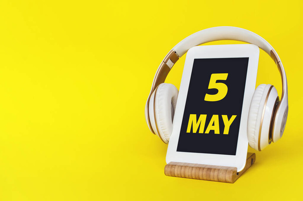 May 5th. Day 5 of month, Calendar date. Stylish headphones and modern tablet on yellow background. Space for text. Concept education, technology, lifestyle. Spring month, day of the year concept - 写真・画像