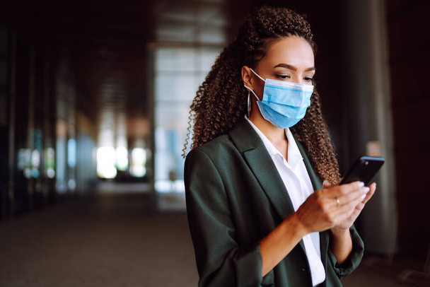 Portrait of a business woman wearing a protective mask with phone solves work issues. Work during coronavirus pandemic. Covid-2019. - Foto, Bild