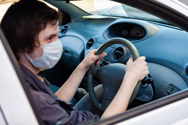 Koruyucu tıbbi maskeli genç bir adam araba kullanıyor. Maskeli bir adam. Koronavirüs salgını sırasında güvenlik, salgın covid-19. - Fotoğraf, Görsel