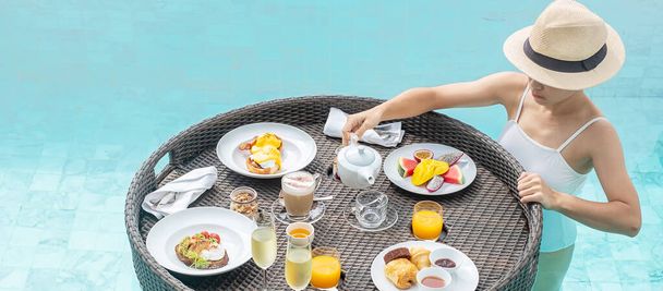 Vrolijke vrouw in wit badpak met Floating Breakfast lade in luxe poolhotel, jonge vrouw met zonnebril genieten in tropische resort. Ontspannen, Exotische zomervakantie, vakantie, vakantie en weekend - Foto, afbeelding