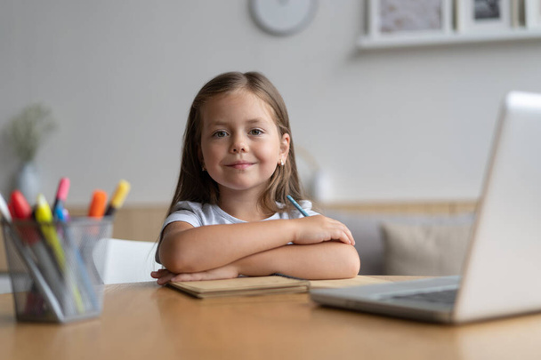 Portrait of happy small pupil learning at home. Smart kid schoolgirl looking at camera, studying remotely online - Фото, зображення