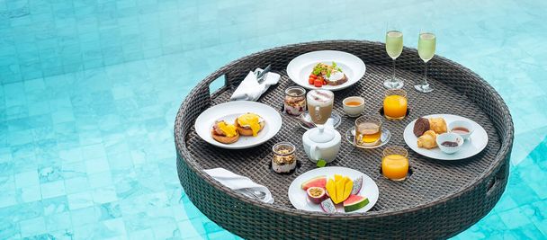 豪華なホテルやトロピカルリゾートヴィラでのスイミングプールでの浮遊朝食トレイ、果物;マンゴー、スイカドラゴンとパッションフルーツ、食べ物、パン、コーヒー、紅茶、ワイン、オレンジジュース。エキゾチックな夏 - 写真・画像