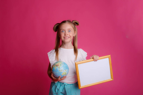 Portret van een meisje met een bol in haar handen en een leeg frame, glimlachende plaats voor tekst Studio op een roze achtergrond - Foto, afbeelding