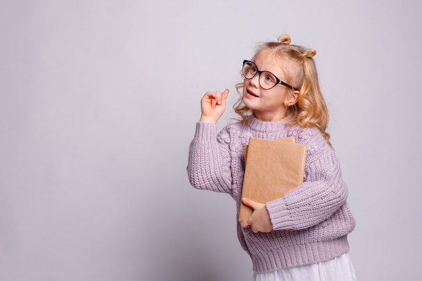 ένα ξανθό κορίτσι προσχολικής ηλικίας με γυαλιά, κρατώντας ένα βιβλίο  - Φωτογραφία, εικόνα