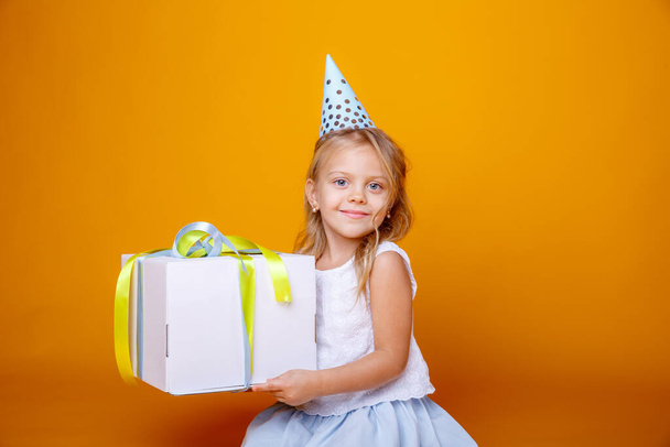 syntymäpäivä tyttö poseeraa lahjapakkauksessa vastaan oranssi studiossa - Valokuva, kuva