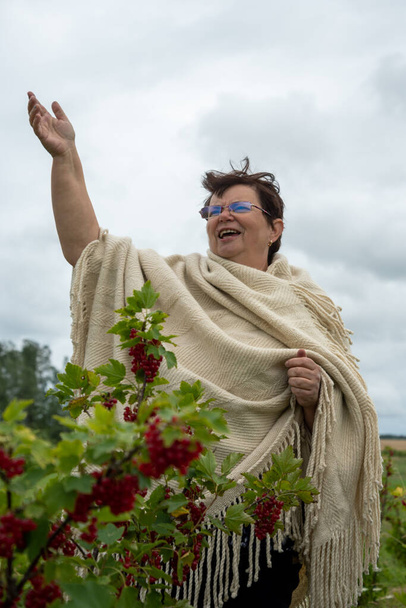 Grandmother screams in countryside at the bush of red currant. - Photo, Image