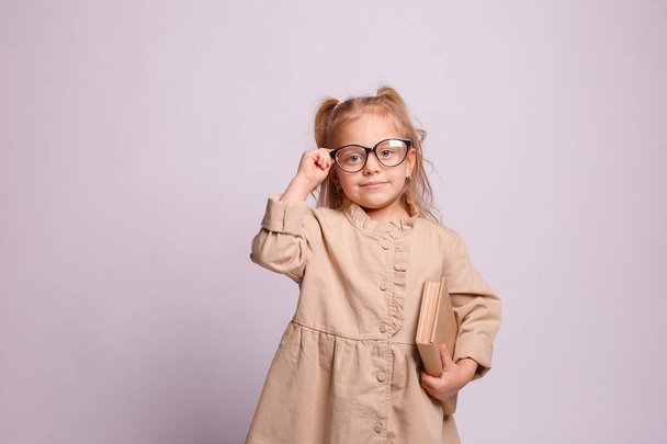little schoolgirl girl in glasses with a book on a gray background.   - Photo, image