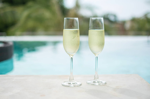 Dwa musujące kieliszki szampana lub prosecco w pobliżu basenu. Letnie podróże, wakacje, wakacje i koncepcja weekendowa - Zdjęcie, obraz