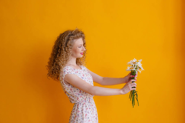 a curly woman holding a bouquet of daisies on a orange background  - Fotó, kép