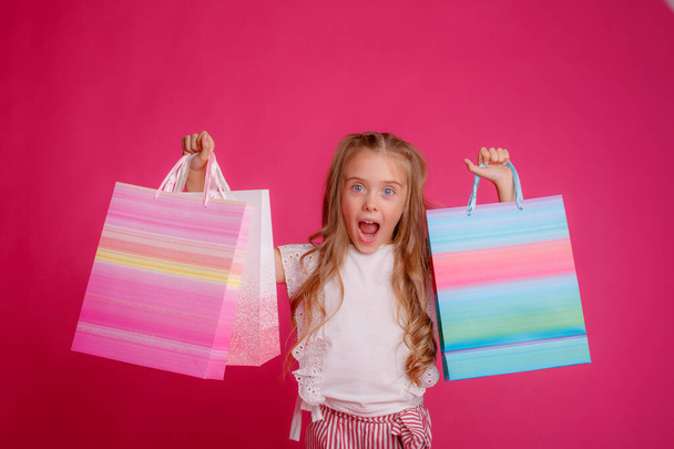 egy kislány egy csomó bevásárló táskák rózsaszín háttér a stúdióban, boldog - Fotó, kép