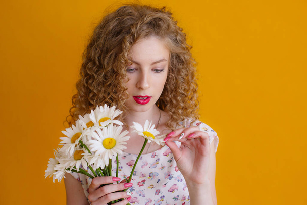 a curly woman holding a bouquet of daisies on a orange background  - Photo, image