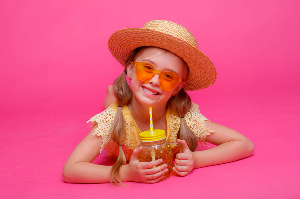 uma menina em óculos de sol, um chapéu de palha e um coquetel está deitado em um fundo rosa - Foto, Imagem