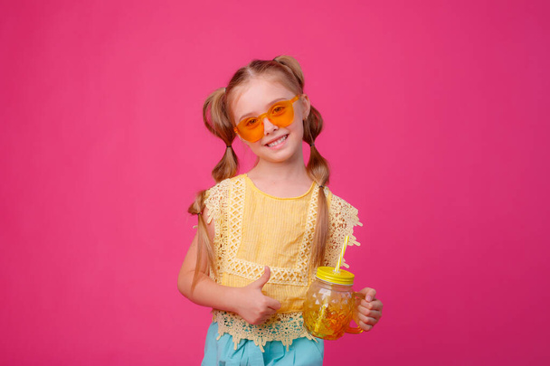 portret małej blondynki w okularach przeciwsłonecznych na różowo ze szklanym słoikiem chłodzącego koktajlu. - Zdjęcie, obraz