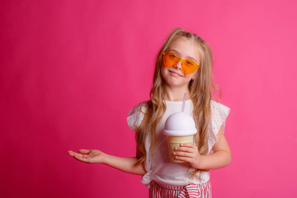 portrait of a little blonde girl in sunglasses on pink with a glass jar of cooling cocktail. - Valokuva, kuva