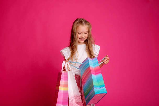 маленька дівчинка з великою кількістю сумки на рожевому тлі в студії, щаслива
 - Фото, зображення