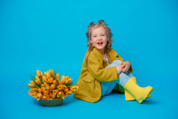 κοριτσάκι με ένα κίτρινο φόρεμα με ένα μπουκέτο λουλούδια σε μπλε φόντο - Φωτογραφία, εικόνα