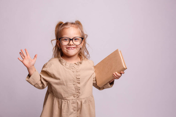 klein schoolmeisje meisje in bril hold boek op een grijze achtergrond.   - Foto, afbeelding