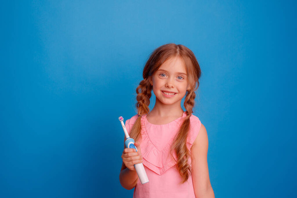 little girl holding electric toothbrush on blue background - Foto, afbeelding