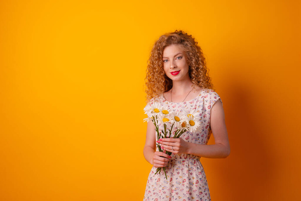 meisje met een boeket madeliefjes op een oranje achtergrond - Foto, afbeelding