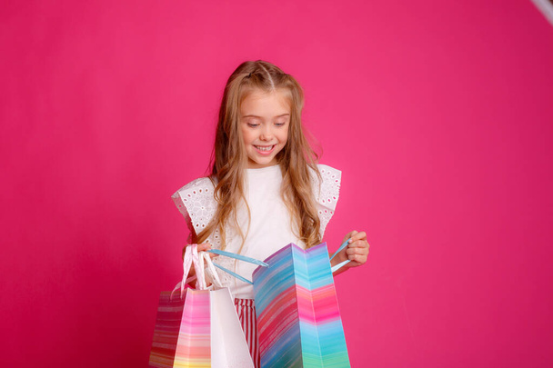 malá holka se spoustou nákupních tašek na růžovém pozadí v ateliéru, šťastná - Fotografie, Obrázek