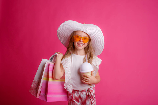 mała dziewczynka z dużą ilością toreb na zakupy na różowym tle w studio  - Zdjęcie, obraz