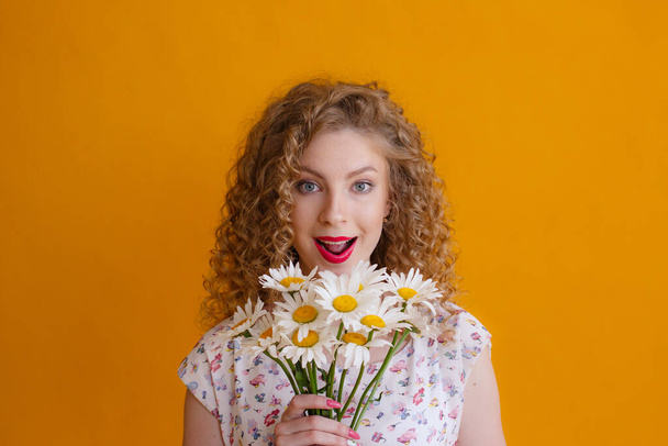 a curly woman holding a bouquet of daisies on a orange background  - Φωτογραφία, εικόνα