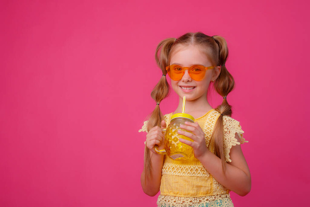 portret małej blondynki w okularach przeciwsłonecznych na różowo ze szklanym słoikiem chłodzącego koktajlu. - Zdjęcie, obraz