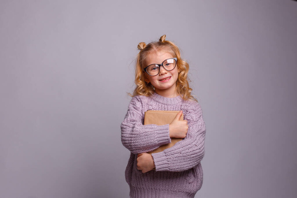 una niña rubia de preescolar en gafas, sosteniendo un libro  - Foto, Imagen